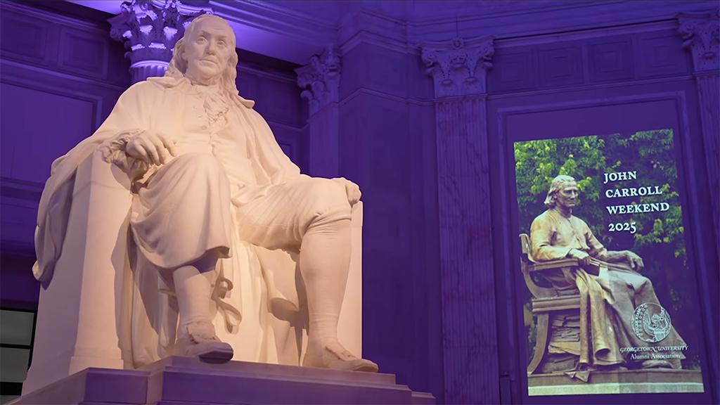 a statue of a man sits next to a banner that says "John Carroll Weekend 2025"